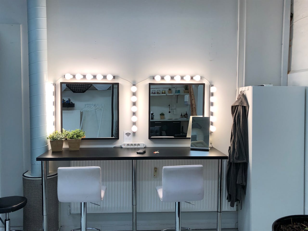 hero-img-02 Brightly lit vanity station with mirrors and minimalist design, ideal for makeup and styling.